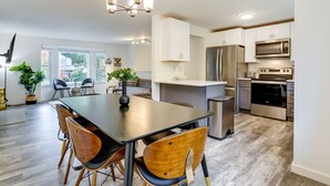 A modern kitchen with white cabinets, stainless steel appliances, and a dining area with a dark table and wooden chairs. - Beautiful Kenmore Retreat Near Marina & Beach! (Kenmore)