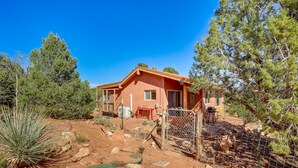 A house with a red exterior, surrounded by a fenced yard with various plants and rocks. - Kanab Studio Escape: Stargaze, Hike, Relax! (Kanab)