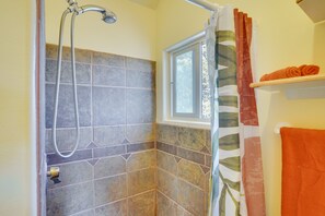 A shower area with a window, a towel rack with an orange towel, and a showerhead. - Kanab Studio Escape: Stargaze, Hike, Relax! (Kanab)