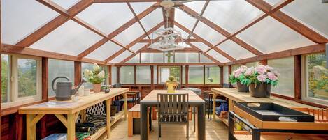 Une serre dotée d’une structure en bois, de tables, de chaises et de plantes en pot.