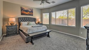 A bedroom with a tufted headboard bed, a bench, two bedside tables with lamps, a ceiling fan, and large windows with blinds. - Retreat w/ Spacious Patio & Superstition Mtn Views (Gold Canyon)
