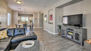 A modern living room with a sectional sofa, a flat-screen TV, and a dining area in the background. - Retreat w/ Spacious Patio & Superstition Mtn Views (Gold Canyon)