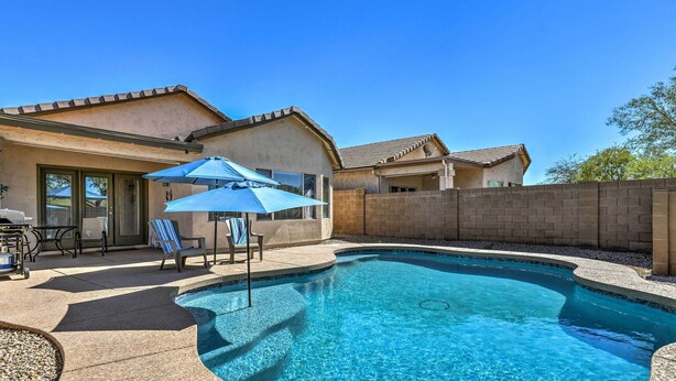 A swimming pool with a curved edge, surrounded by a patio area with chairs and an umbrella. - Retreat w/ Spacious Patio & Superstition Mtn Views (Gold Canyon)
