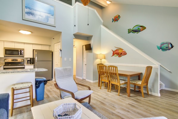 A modern kitchen with a built-in microwave and refrigerator, a dining area with a wooden table and chairs, and a staircase with a fish mural on the wall.