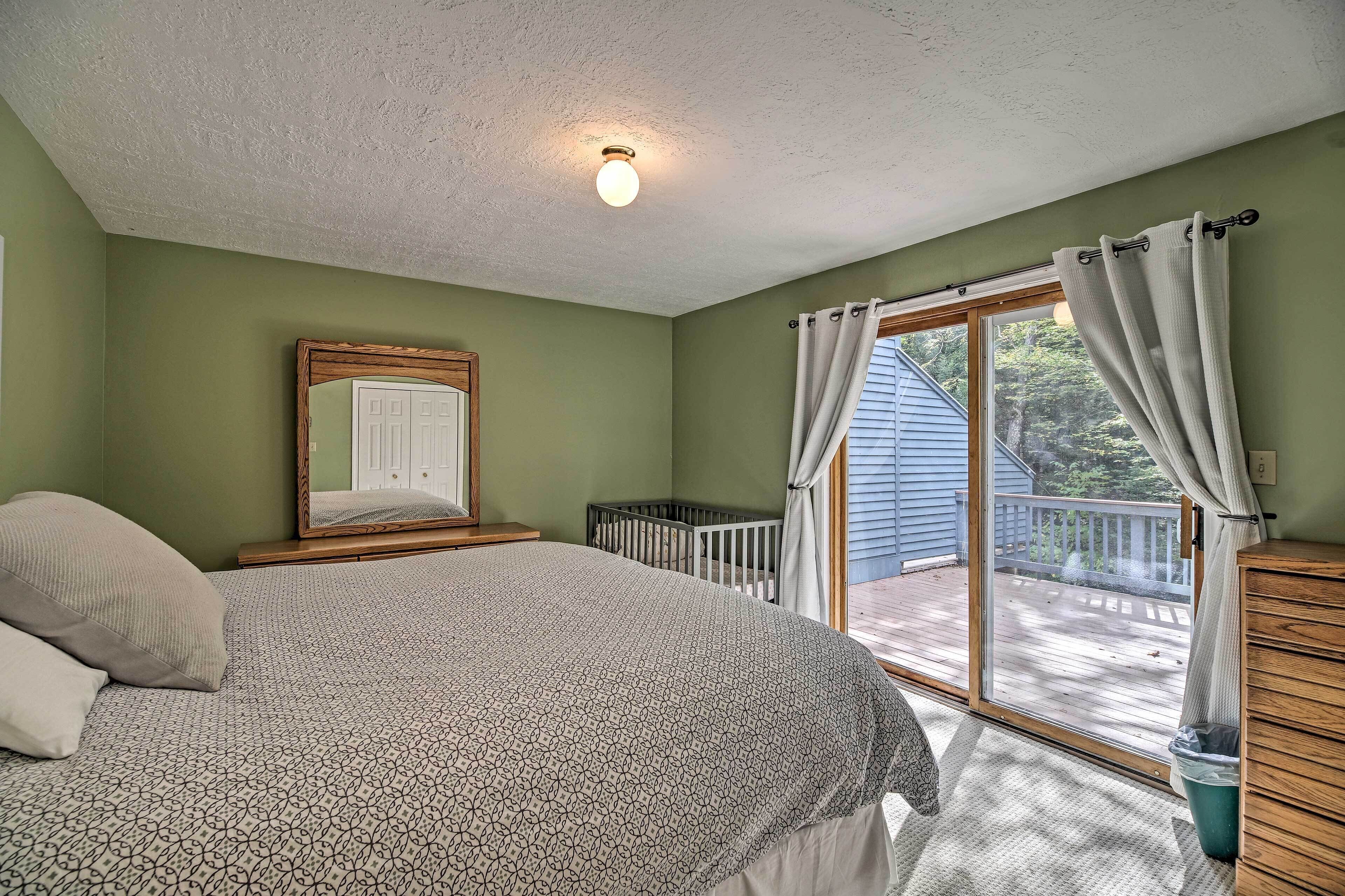 A bedroom with a bed, a crib, a window with curtains, and a view of a deck.