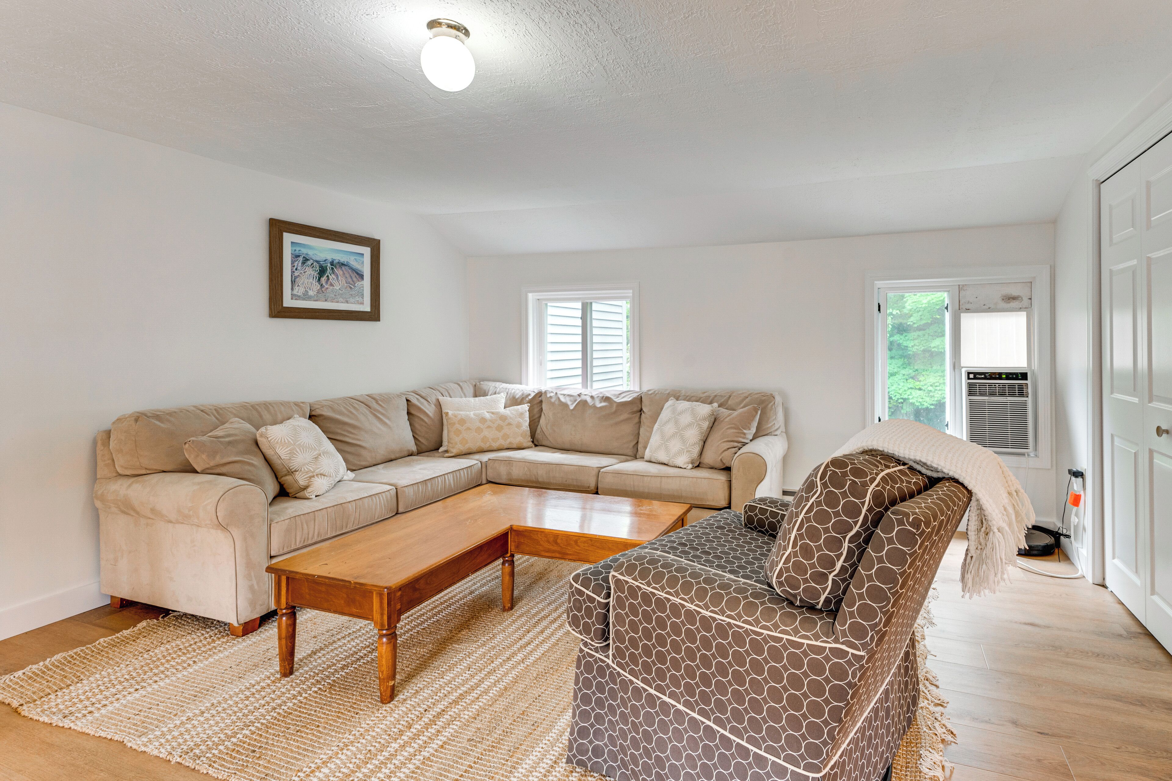 A living room with a beige sectional sofa, a patterned armchair, a wooden coffee table, and a woven rug.