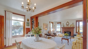 A spacious living room with a fireplace, wooden beams, a dining table with chairs, and a chandelier. - Vintage Charlevoix Home w/ Deck Near Round Lake! (Charlevoix)