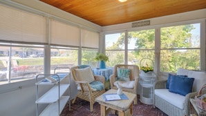 A sunroom with wicker furniture, a small table, and a bench. - Vintage Charlevoix Home w/ Deck Near Round Lake! (Charlevoix)