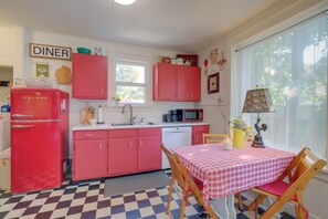 Une cuisine au style rétro, avec un réfrigérateur rouge, une enseigne de restaurant et une nappe à carreaux.