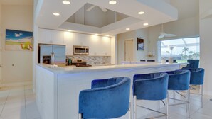 A modern kitchen with a central island, bar stools, and a ceiling fan. - Canal-view Oasis w/ Grill in Cape Coral! (Cape Coral)