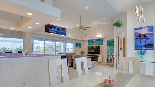 A modern kitchen with a central island, a dining area with a glass-top table, and a living space with a TV and artwork. - Canal-view Oasis w/ Grill in Cape Coral! (Cape Coral)