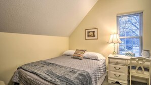 A bedroom with a bed, a nightstand, a lamp, a window with blinds, and a picture on the wall.