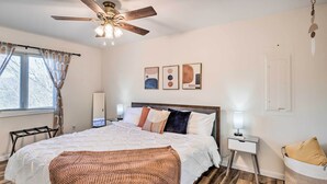 Une chambre à coucher comprenant un lit, un ventilateur de plafond, une table de chevet, une lampe et une œuvre d’art accrochée au mur.