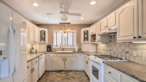 Une cuisine avec des armoires blanches, un fourneau et un ventilateur de plafond.