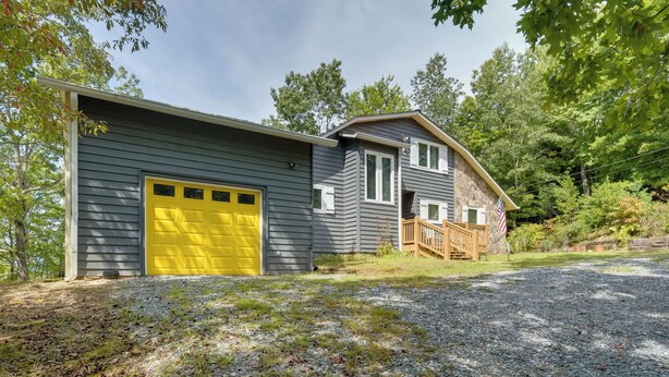 Une maison à deux étages avec une porte de garage jaune, une façade en pierre et une terrasse en bois.