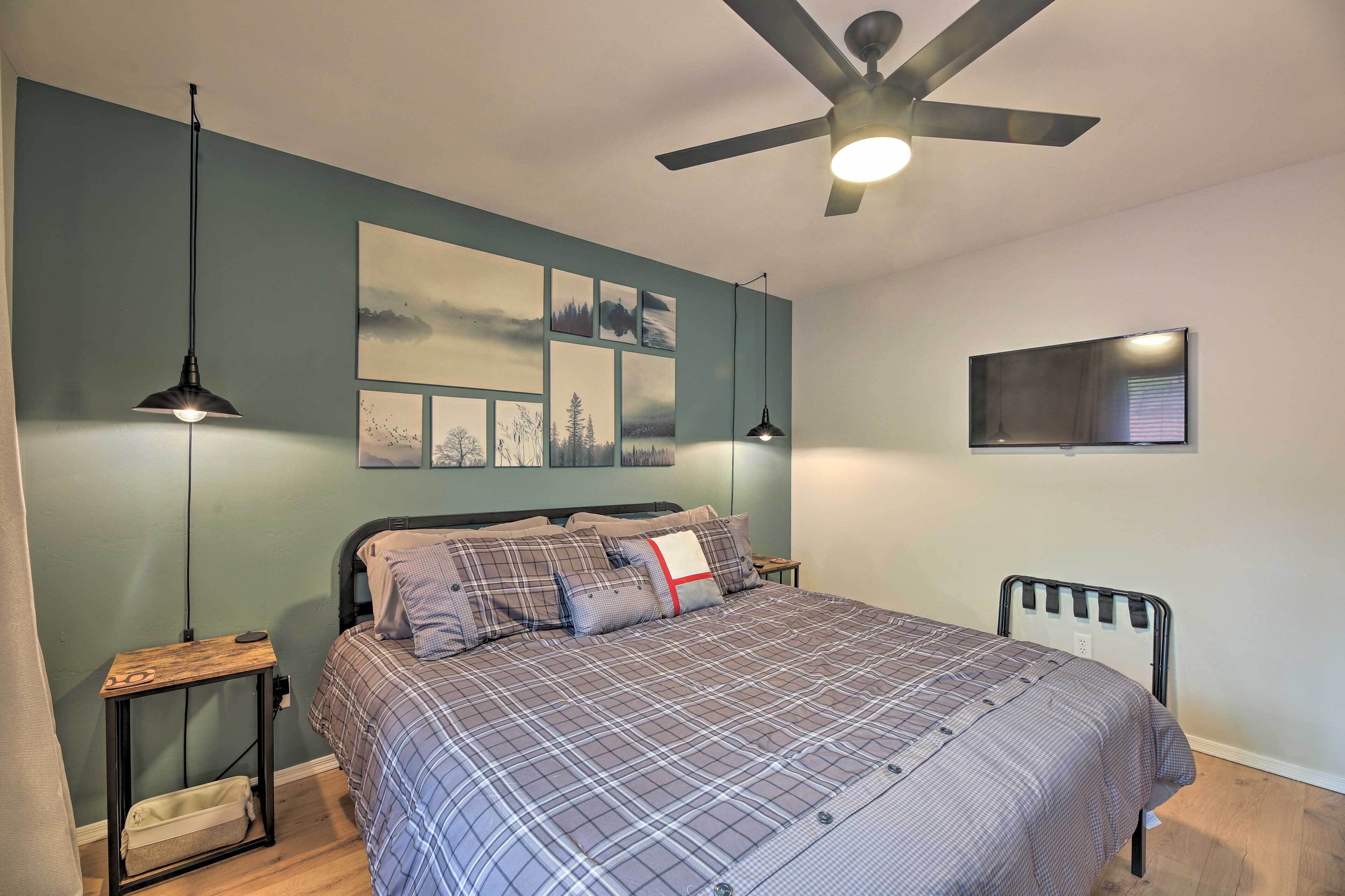 Une chambre à coucher comprenant un lit, deux tables de chevet, un ventilateur de plafond et des œuvres d’art accrochées au mur.