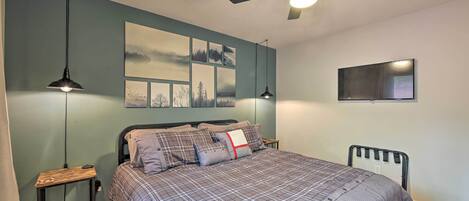 Une chambre à coucher comprenant un lit, deux tables de chevet, un ventilateur de plafond et des œuvres d’art accrochées au mur.