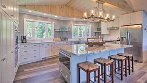 A spacious kitchen with a large island, wooden ceiling beams, and a modern chandelier. - Lush Gilbert House w/ Outdoor Oasis on Lake Murray (Gilbert)