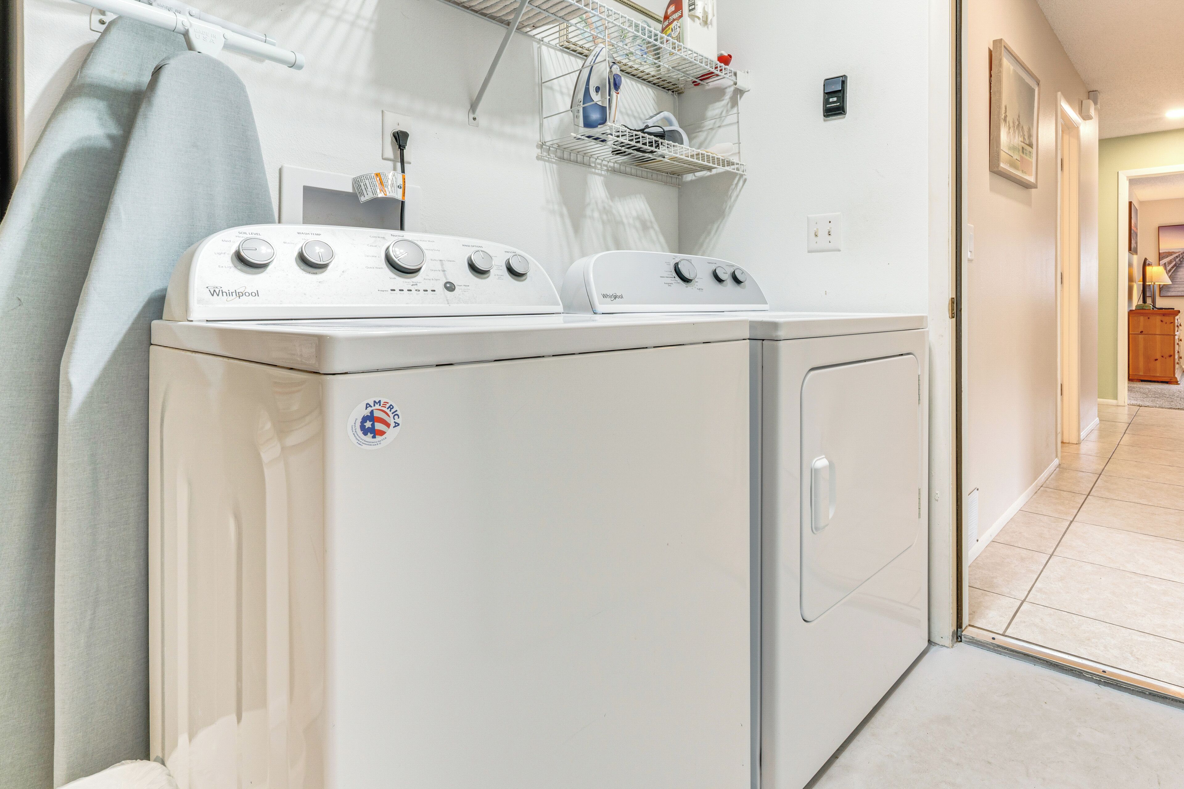 A laundry area with two Whirlpool washers and dryers, a drying rack, and a shelf with laundry supplies.