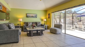 A living room with a sofa, armchair, coffee table, and a glass door leading to an outdoor patio.