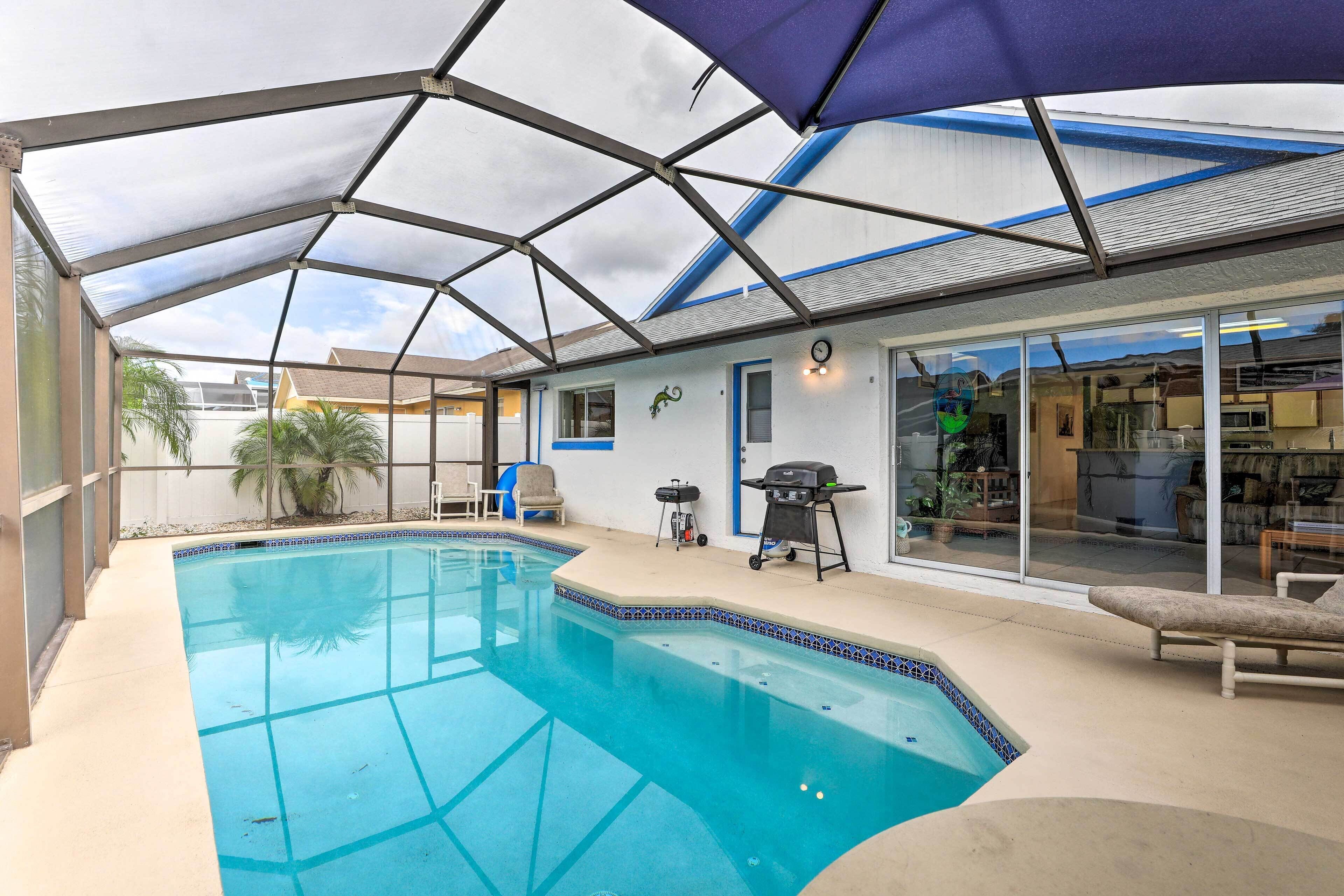 Una piscina con un porche cubierto, una parrilla de barbacoa y una zona de estar con una silla y una mesa.