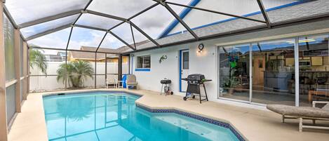 A swimming pool with a covered patio area, a barbecue grill, and a seating area with a chair and a table.
