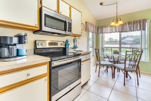 Una cocina con microondas, horno, cafetera y comedor con sillas y mesa.