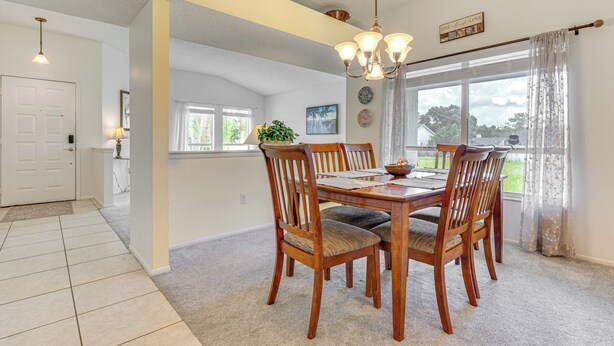 A dining area with a wooden table and chairs, a chandelier, and a view of the outdoors through large windows.