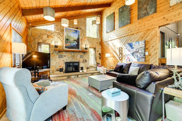 A cozy cabin interior with a stone fireplace, wooden walls, a comfortable seating area, and a television.