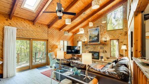 Un salon spacieux doté d’une cheminée en pierre, d’un plafond en bois et de grandes fenêtres.