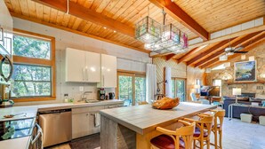 Une cuisine moderne dotée d’un grand îlot central, de poutres apparentes en bois au plafond et de grandes fenêtres.
