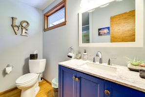 A bathroom with a white toilet, a blue vanity with a sink, a mirror, and a 'LOVE' decoration on the wall.