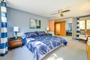 A bedroom with a bed, nightstands, a ceiling fan, a large mirror, and a view of a bathroom.