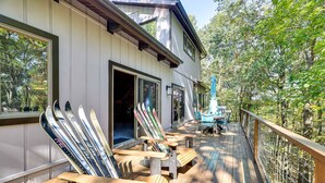 Une terrasse en bois, avec des chaises et des paires de skis, donnant sur une zone boisée.