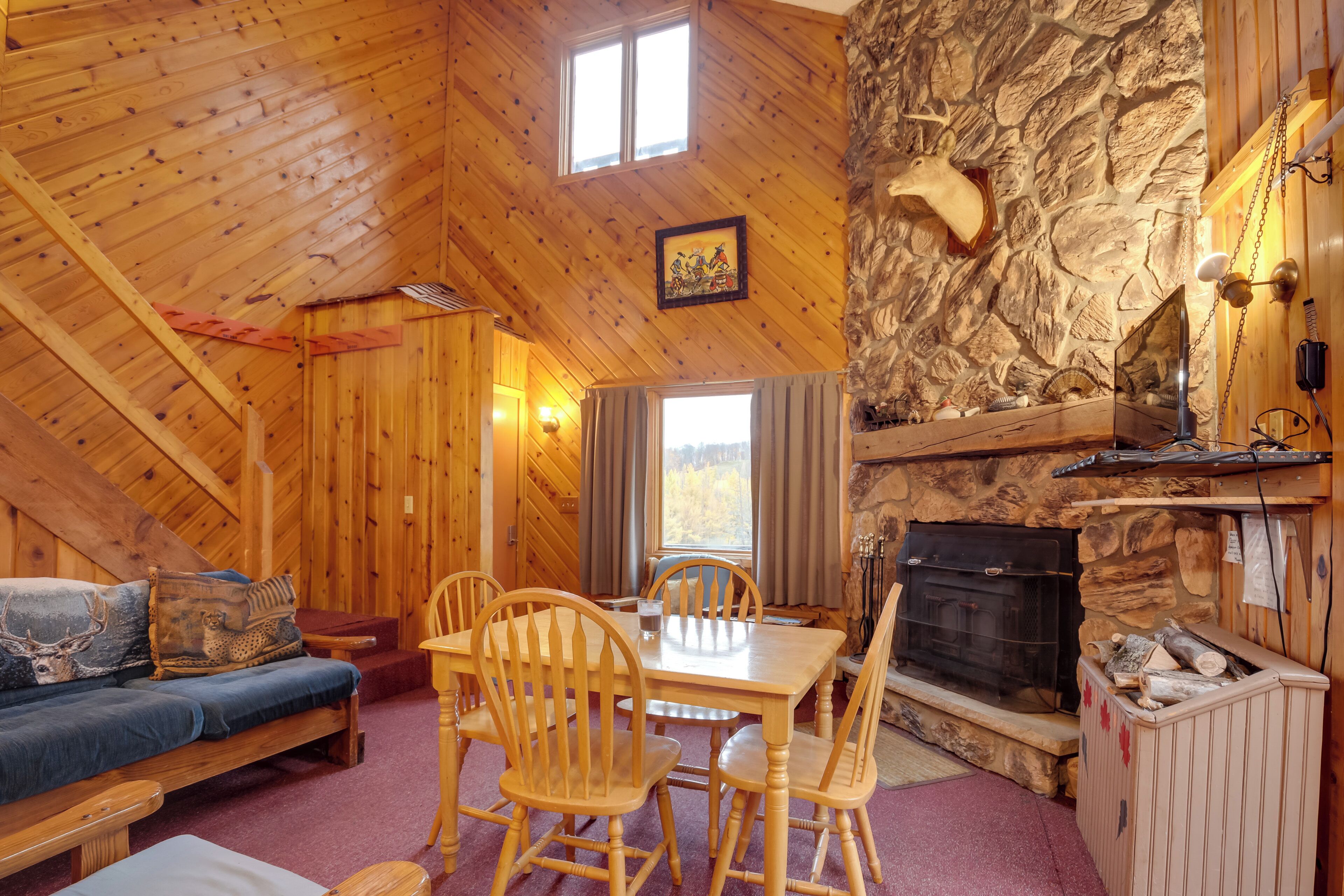 L’intérieur chaleureux d’un chalet avec une cheminée en pierre, des meubles en bois et une vue magnifique par la fenêtre.