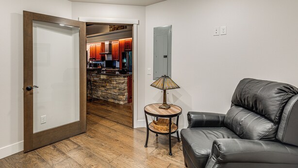 A living room with a leather sofa, a small wooden side table with a lamp, and a kitchen visible through an open door. - Mendenhall Valley Escape w/ Furnished Deck! (Juneau)