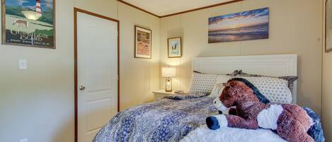 A bedroom with a bed, a ceiling fan, a nightstand with a lamp, and wall decorations including a poster and a painting.