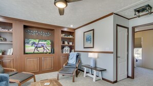 Ein Wohnzimmer mit Fernseher, einem Sessel, einem Couchtisch und einem Bücherregal.