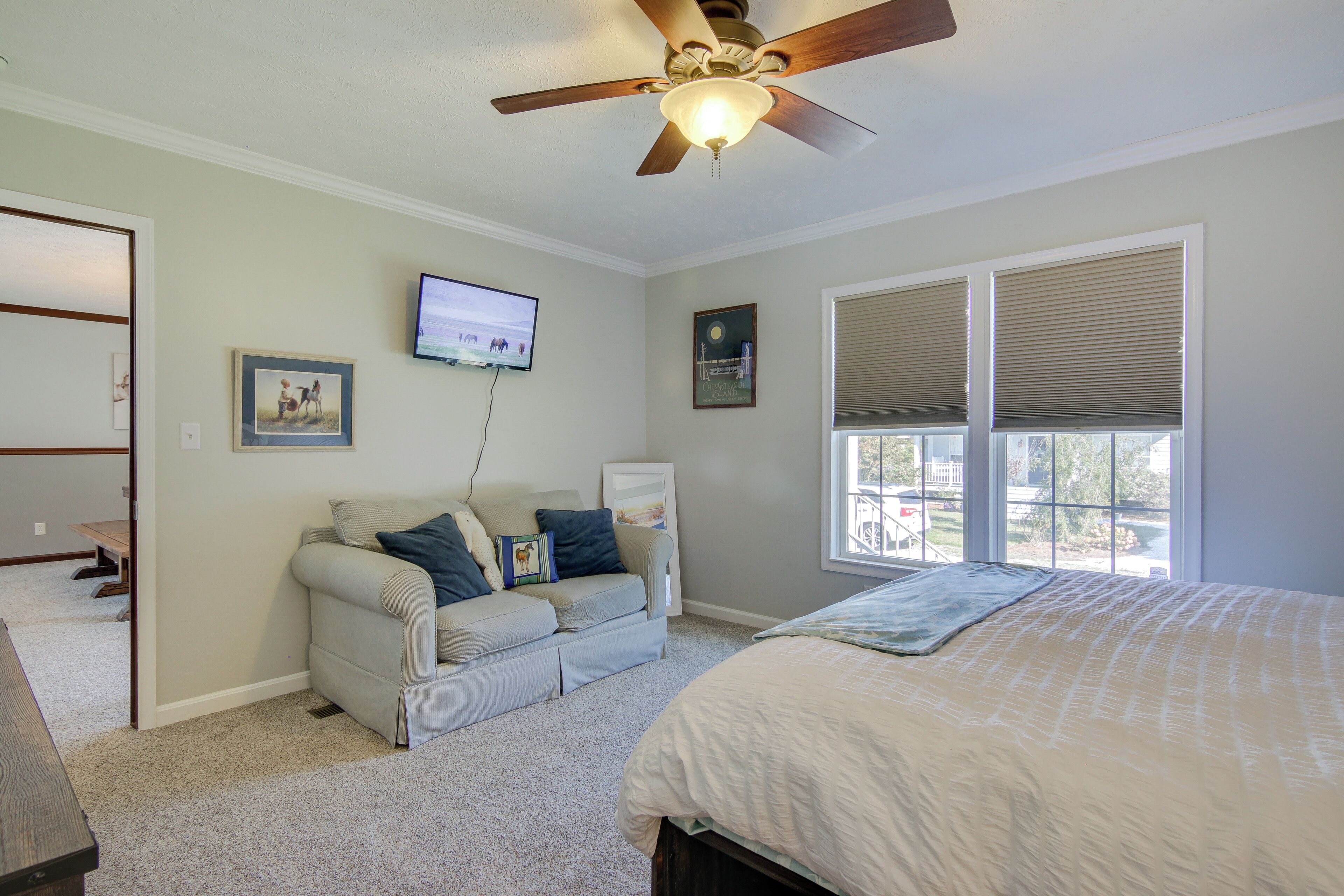 A bedroom with a bed, a ceiling fan, a window with blinds, a television, and a couch.