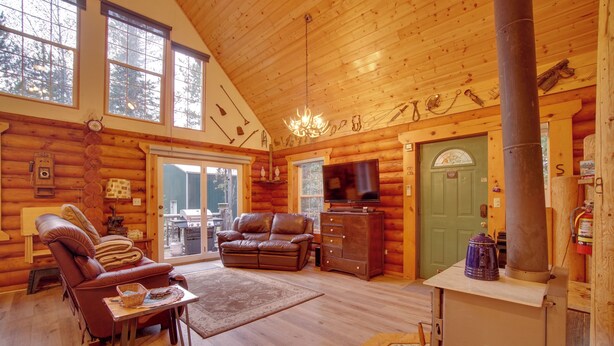 A log cabin interior with a fireplace, leather furniture, and a large window.