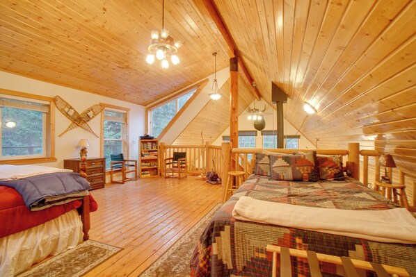 A cozy attic bedroom with wooden floors, a large bed, a desk, and a window overlooking the outdoors.