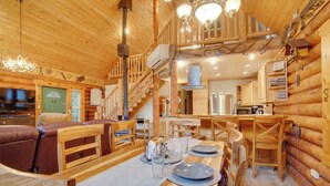 A log cabin interior with a dining area, a staircase, and a kitchen.