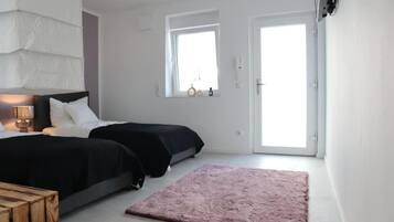Un dormitorio con dos camas, una ventana, una puerta y una alfombra pequeña.