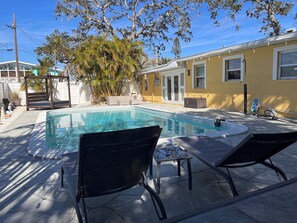 Ein Schwimmbecken mit Liegestühlen, einer Pergola und einem weißen Zaun.