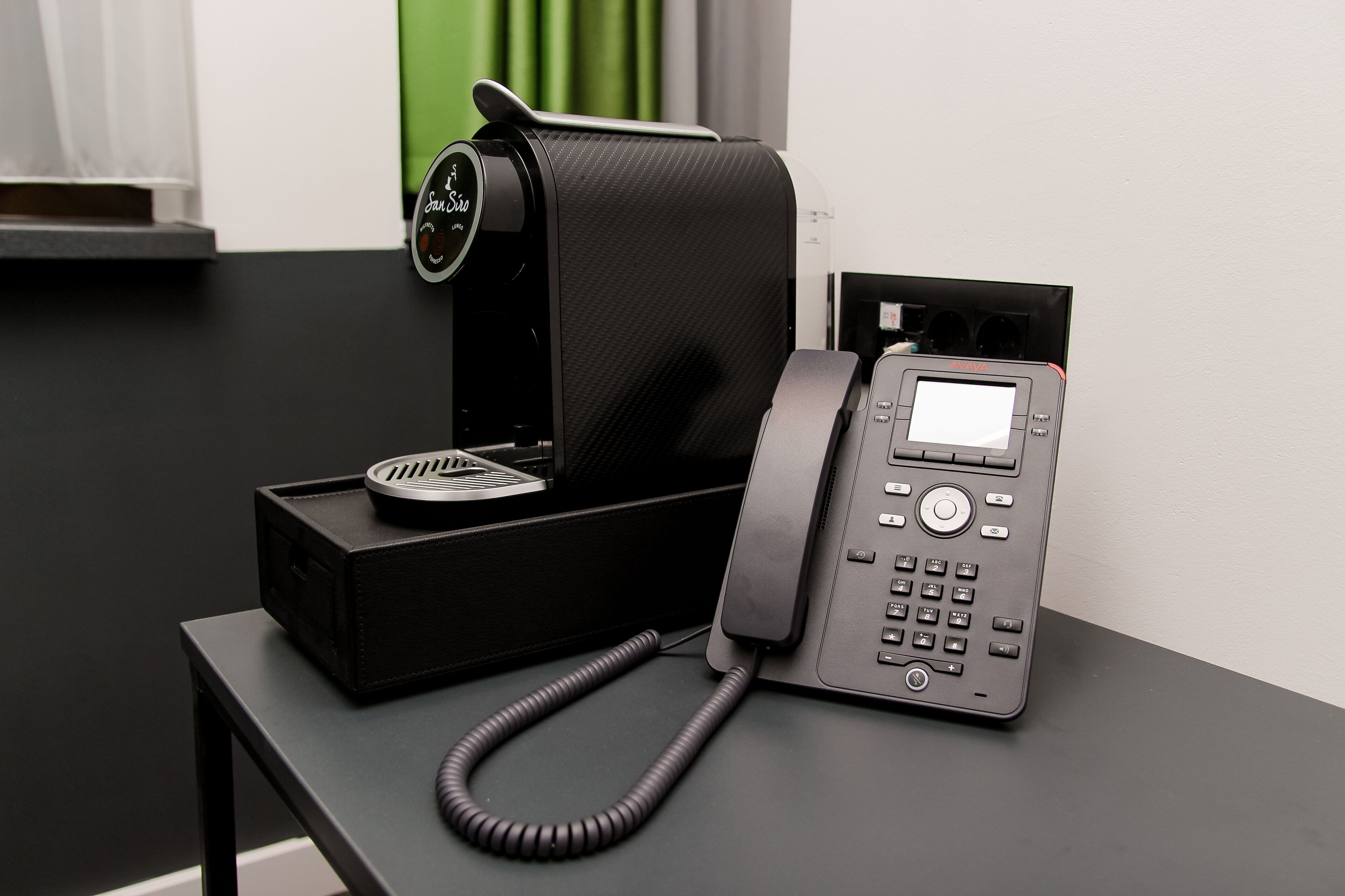 Ein schwarzes Telefon mit Kabel, ein schwarzer Lautsprecher und eine schwarze Box auf einem schwarzen Tisch.