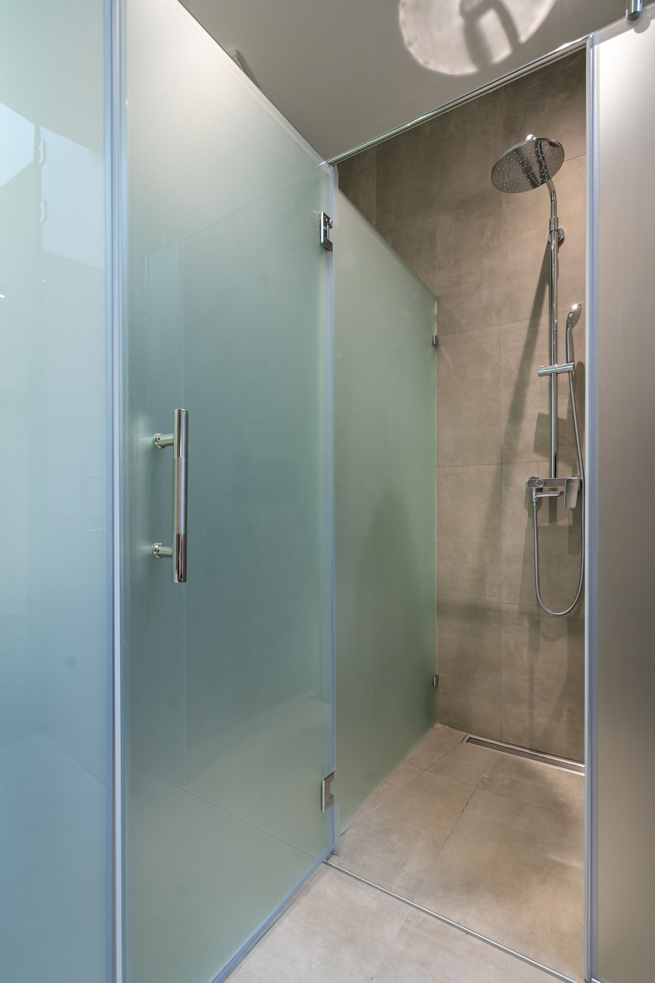 A glass-enclosed shower area with a handheld showerhead and a wall-mounted faucet.