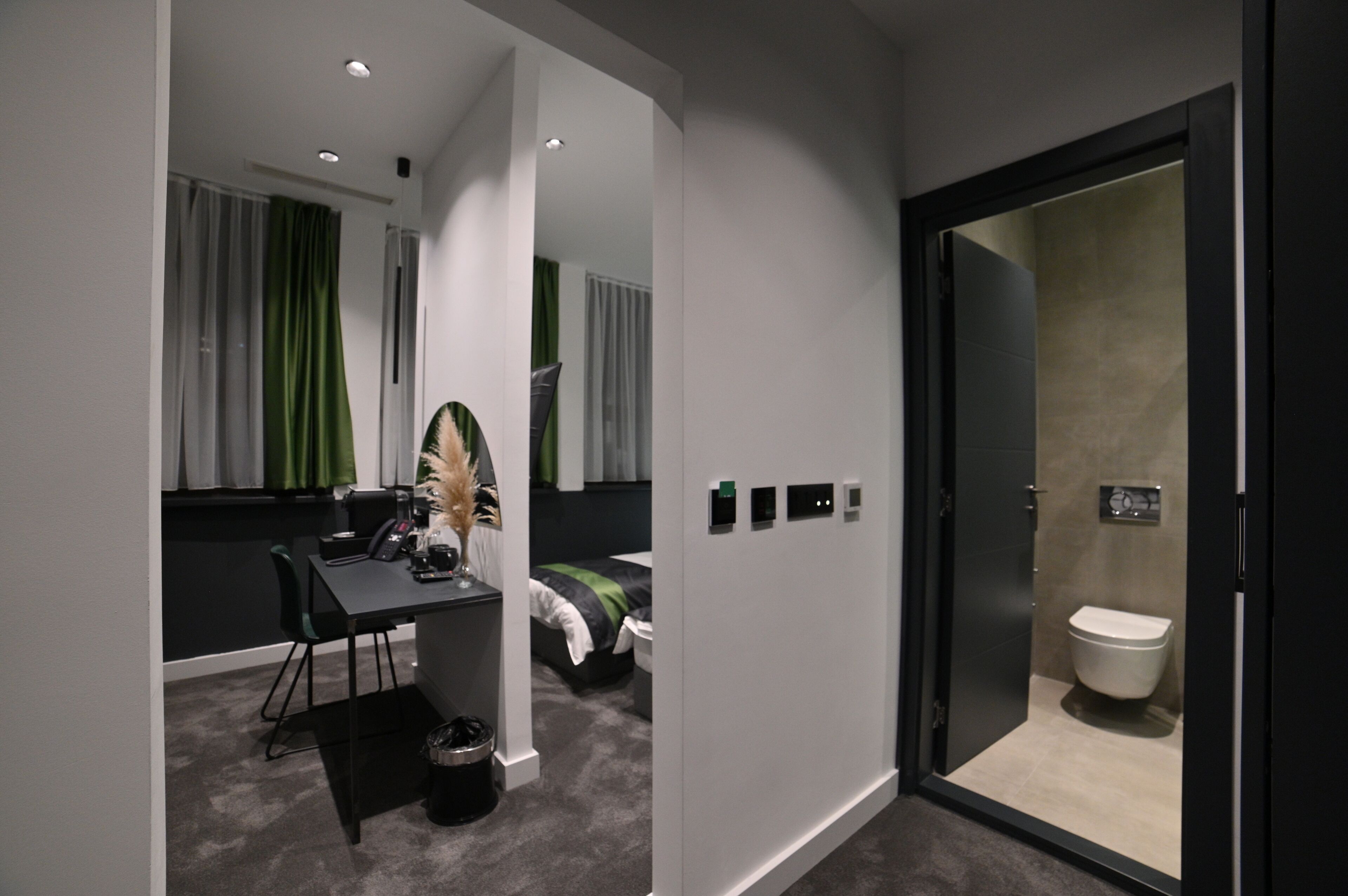 A modern hotel room with a desk, chair, and a bed with green curtains.