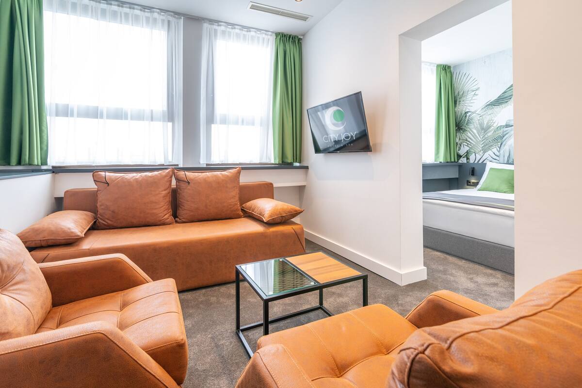 Uma sala de estar moderna com um sofá de couro, uma mesa de centro de vidro e uma TV fixada na parede.
