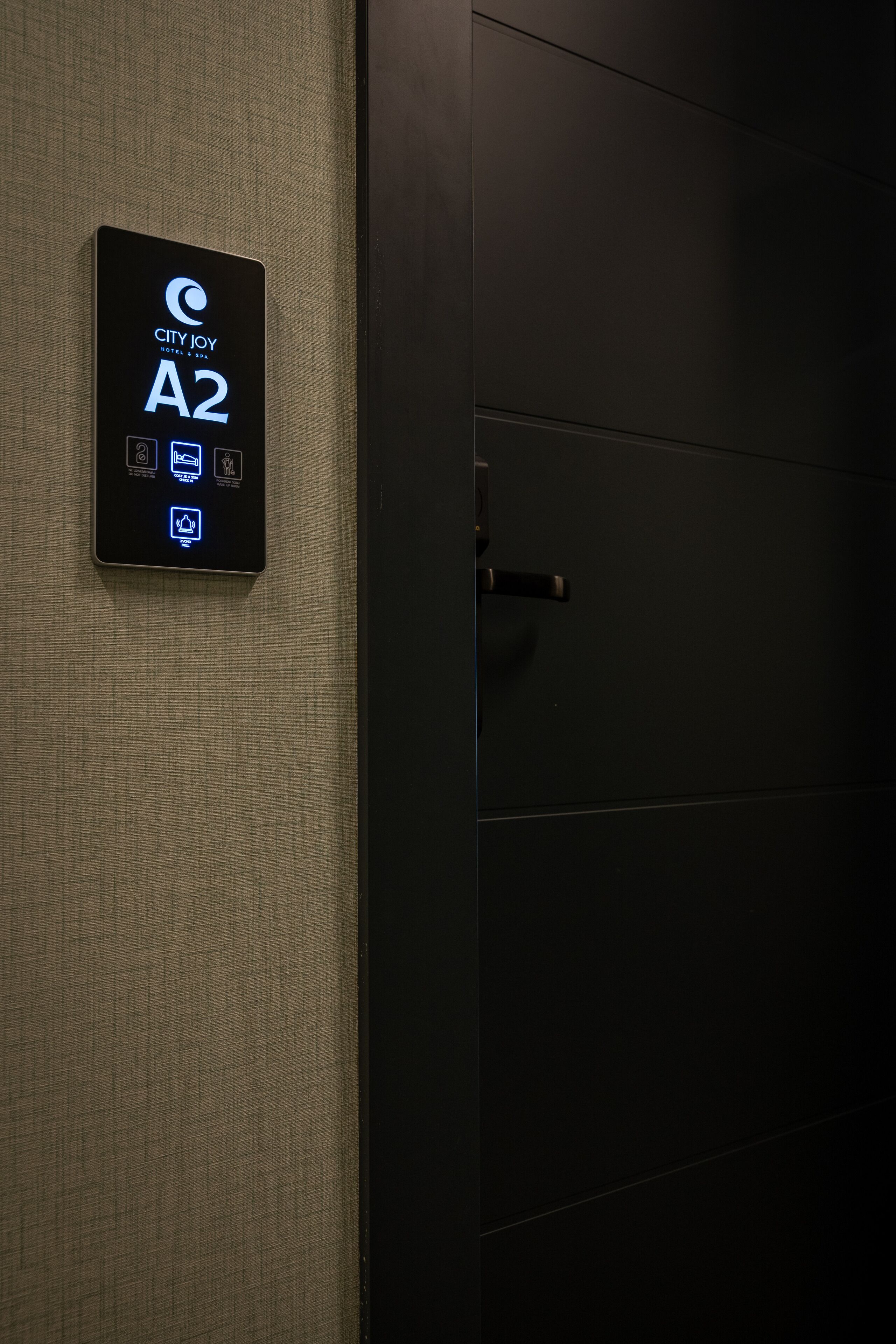 A digital sign indicating City Joy Hotel, room A2, with icons for amenities like Wi-Fi, a desk, and a bed.