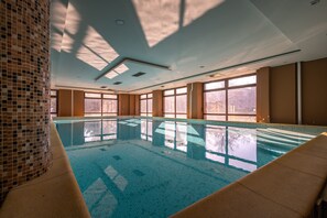 Une piscine intérieure à l’eau claire, dotée de grandes fenêtres et d’un mur recouvert de carreaux.
